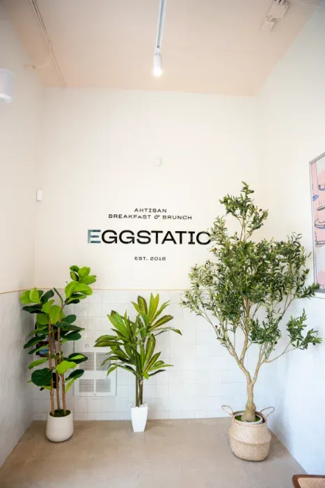 Eggstatic "Artisan Breakfast & Brunch — Est. 2018" entry wall and large plants at the London Ontario location