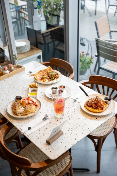 Brunch spread of pancakes, eggs benedict and waffles on a sunny window-side table at Eggstatic Scarborough