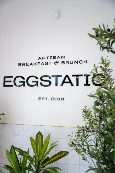 Eggstatic "Artisan Breakfast & Brunch — Est. 2018" wall sign with olive plant at Eggstatic London Ontario