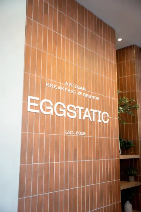 Eggstatic "Artisan Breakfast & Brunch — Est. 2018" wood-tile signage at the Oakville location