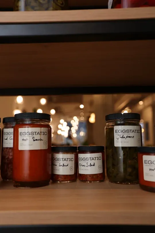 Shelf of Eggstatic-labelled hot sauce, salsa, olive salad and jalapeño preserves at Eggstatic Montreal