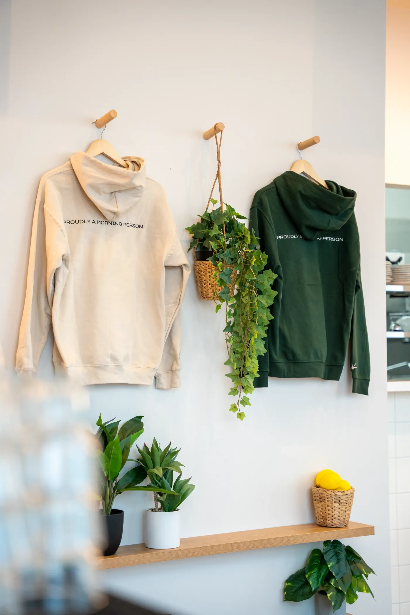 Eggstatic “Proudly a Morning Person” hoodies displayed on the wall with a hanging plant
