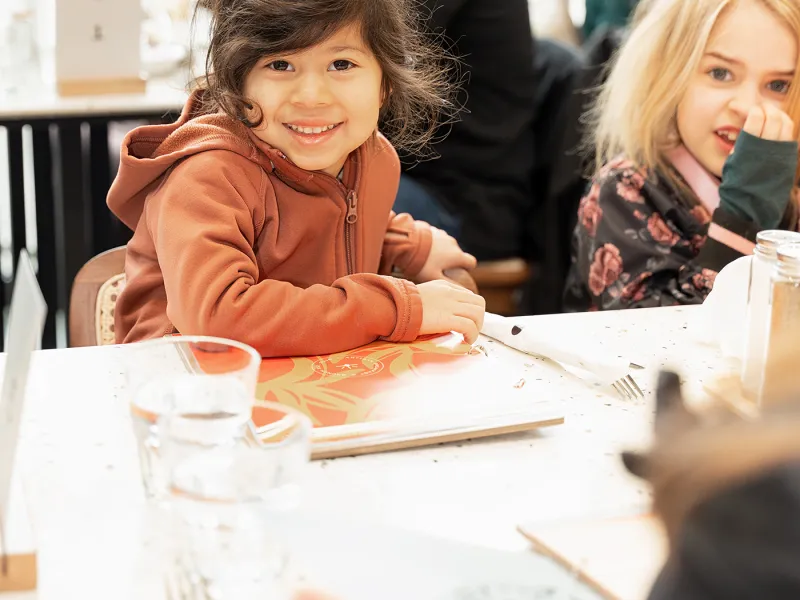 Child smiling at a family brunch table at Eggstatic
